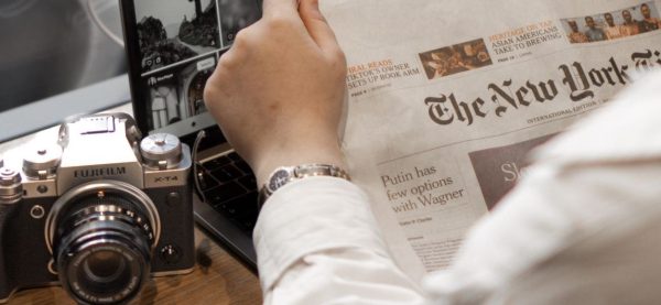 person reading a newspaper and using a laptop and a camera